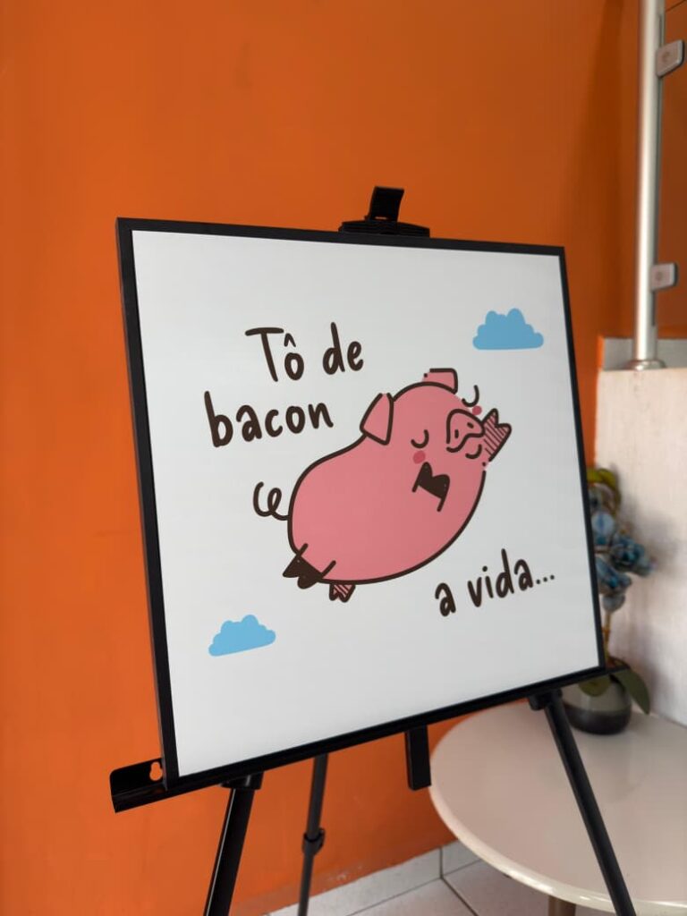 Foto de um quadro decorativo da Stalo Decor.
O quadro é quadrado com moldura preta, e a imagem traz um porquinho em expressão serena com a frase "tô de bacon a vida".