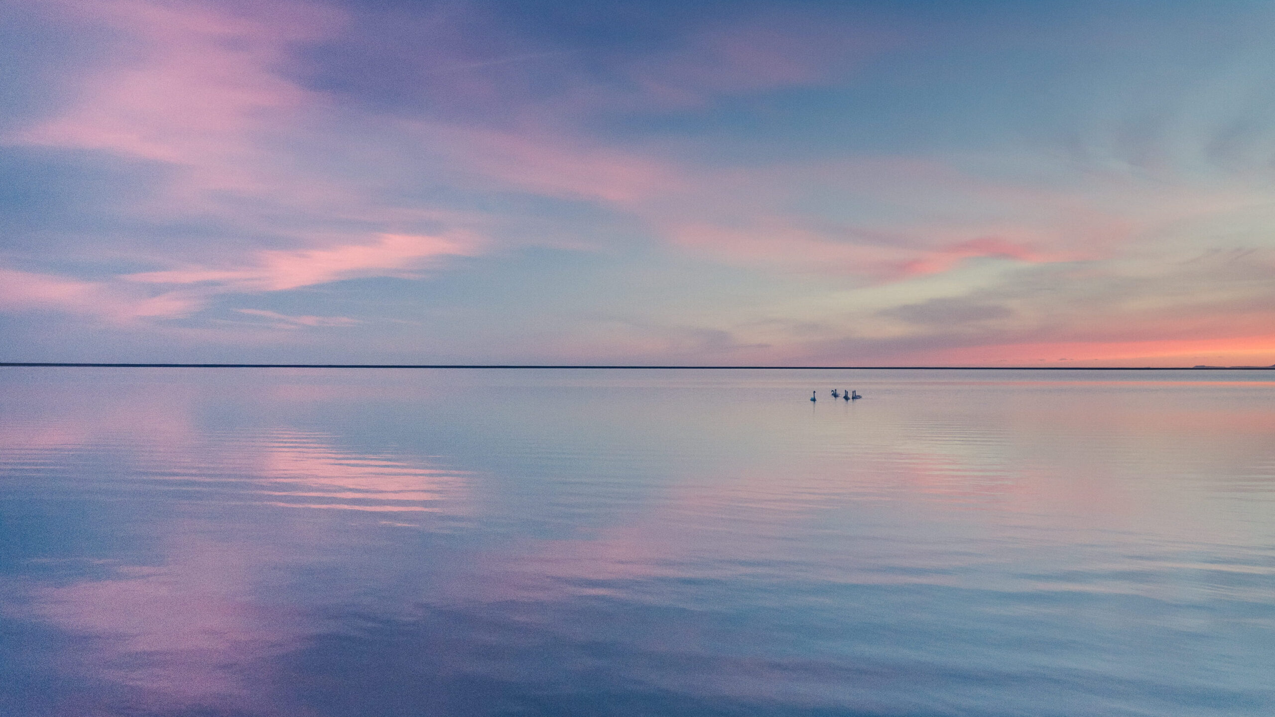 Foto de um lago e do céu. O lago reflete o céu em um fim de tarde, que possui uma mistura das cores azul, lilás e laranja. A foto passa as sensações de calma e tranquilidade.

