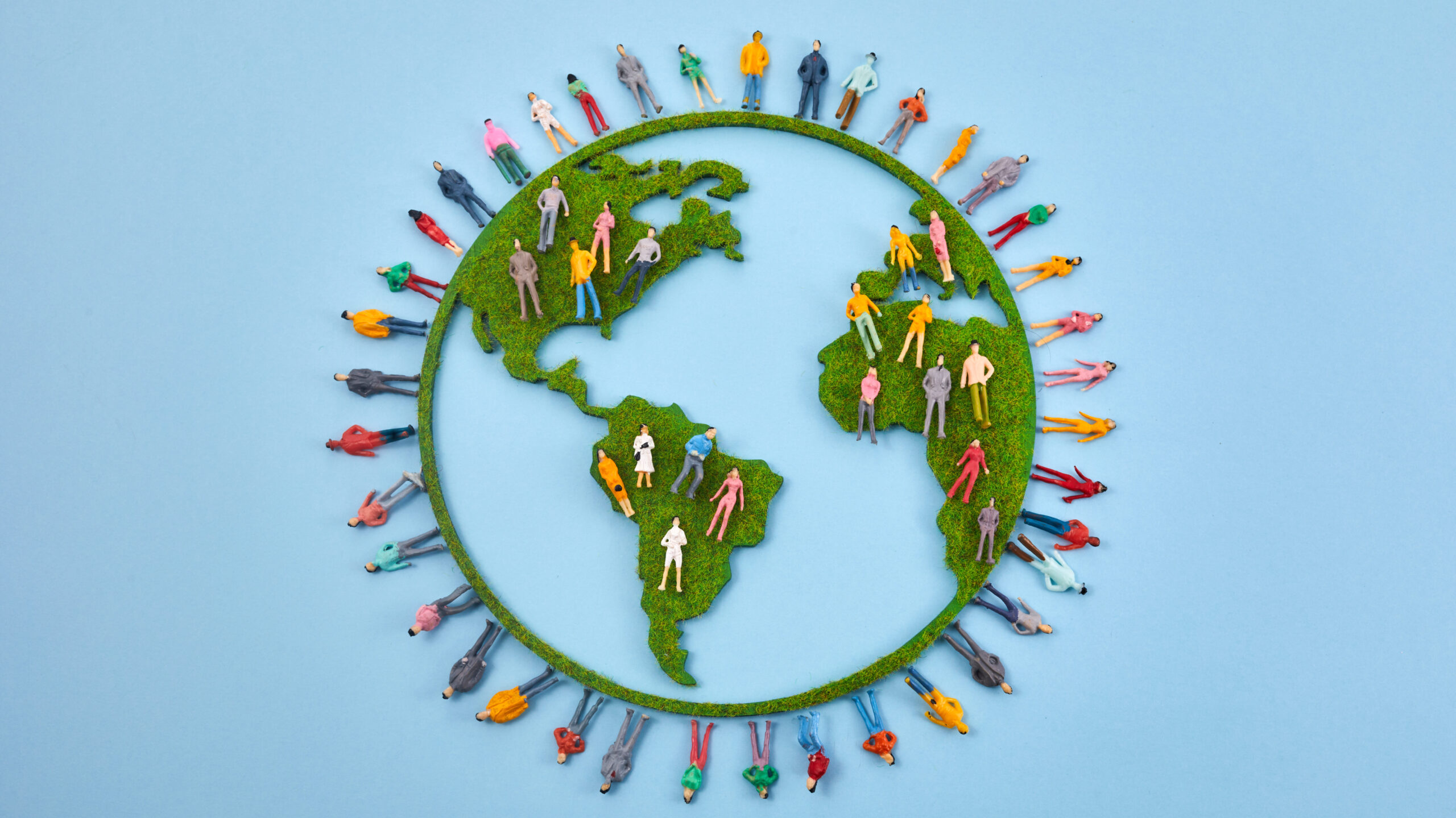 planeta terra com continentes cobertos de grama verde e miniaturas de pessoas ao redor, representando a sustentabilidade e a diversidade humana.